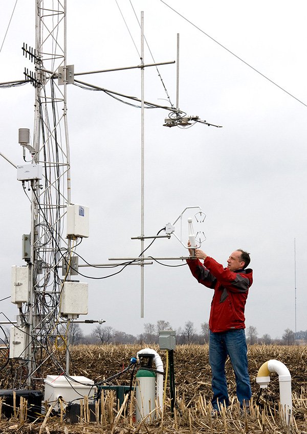 A man wearing a red jacket examines climatology equipment in a field.