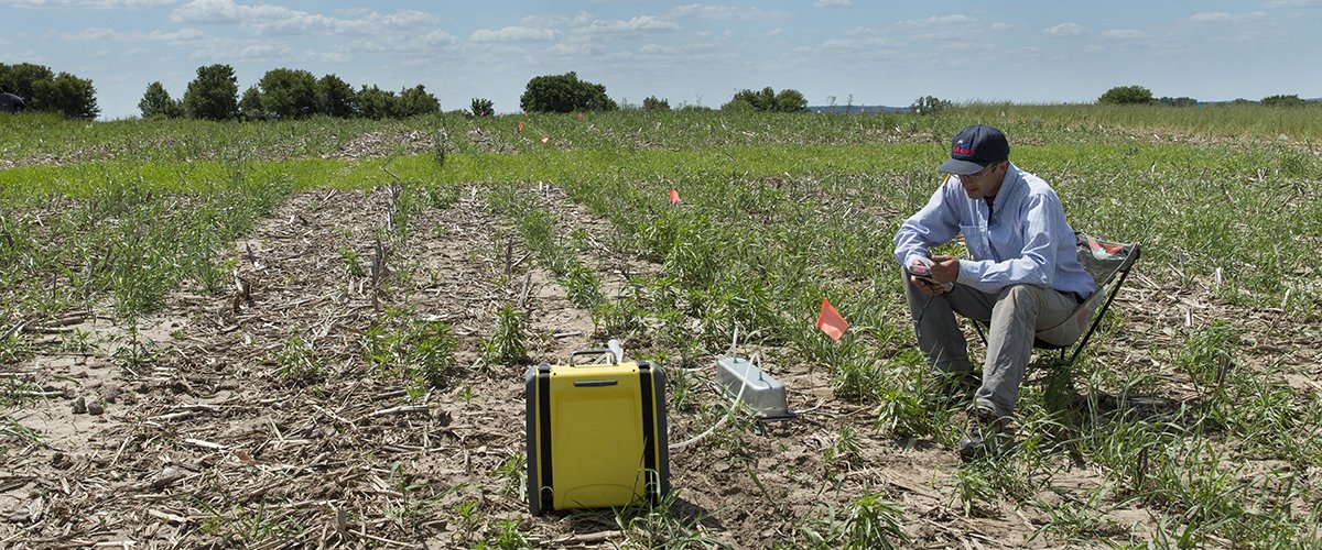 A man sitting in a field looks at a soil sensor